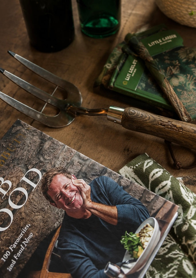 Father's Day collection, a hand fork gardening tool, a leather notebook, and a cookbook on a wooden table. Elegant text reads, “Father’s Day Collection – For the Ones Who Mean the Most,” creating a cosy, masculine, garden-inspired atmosphere.